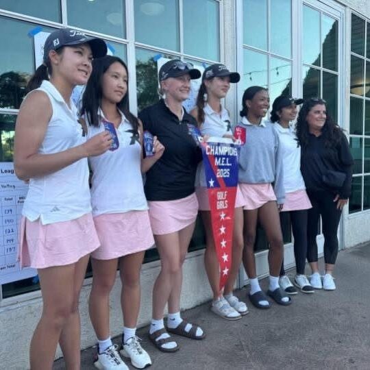 A group of women golfers posing with a trophy outside a building.