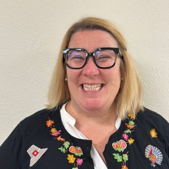 Smiling woman wearing glasses and colorful sweater.